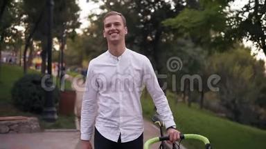 白人微笑的年轻人穿着白色衬衫，骑着自行车在城里的<strong>街道</strong>上<strong>行走</strong>。 一边骑着他的自行车